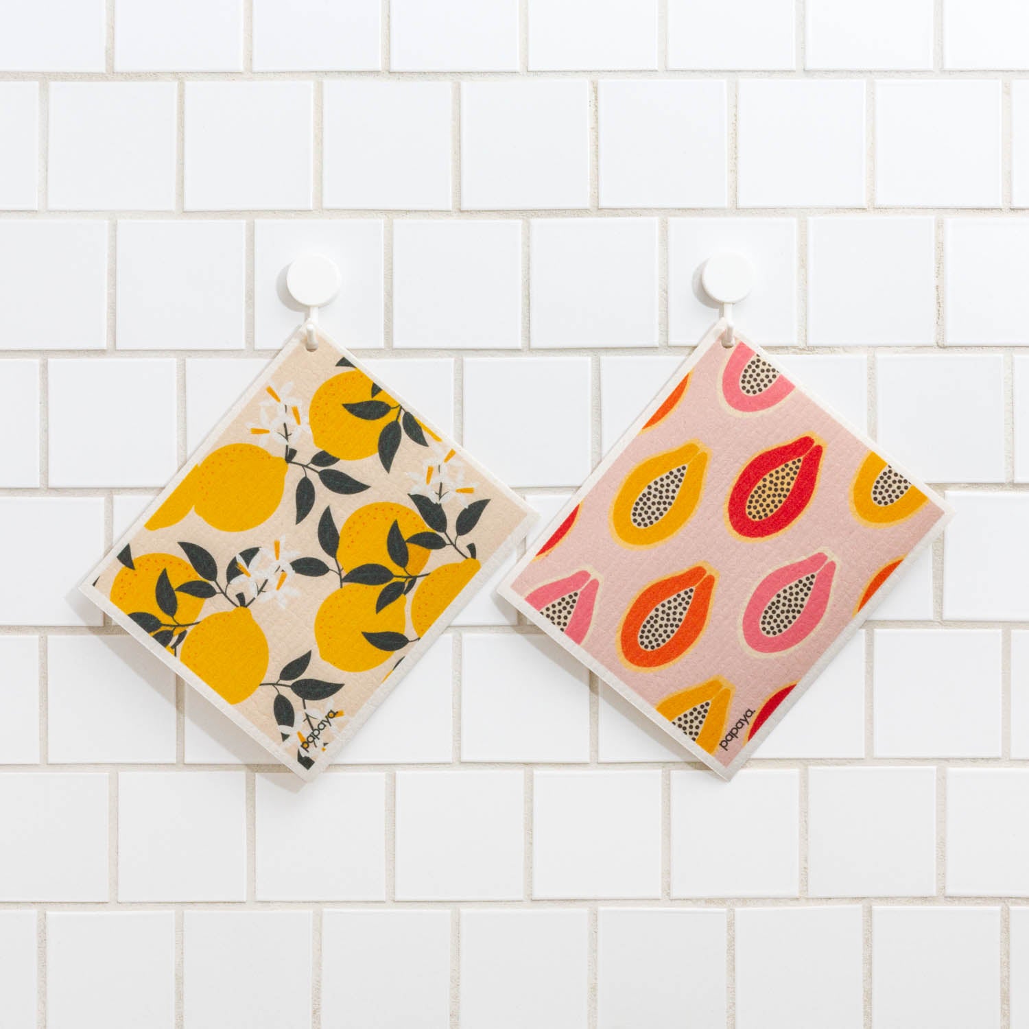 Two reusable paper towels hanging on white tile with cute and colorful lemons and papaya designs