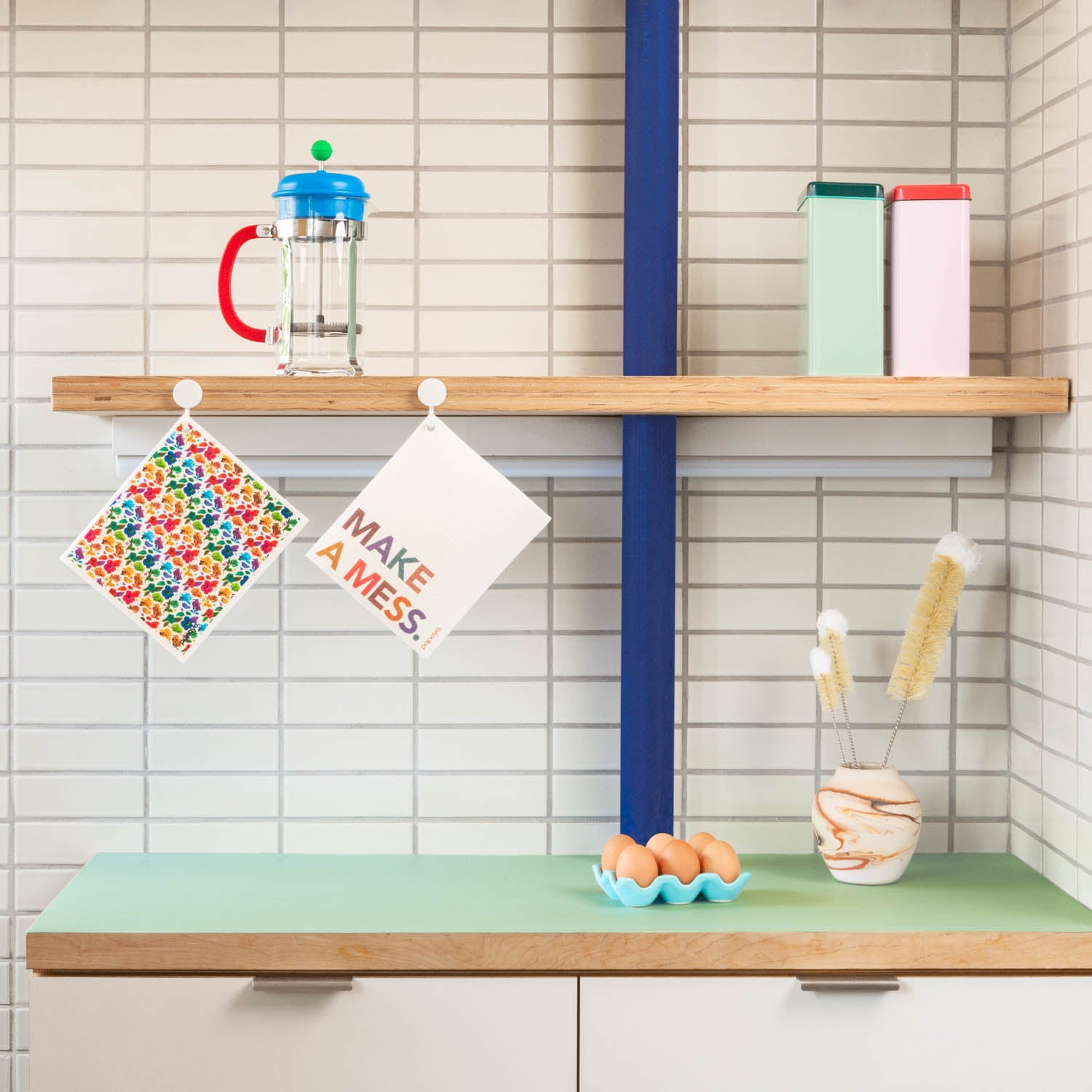 Two reusable paper towels hanging in modern kitchen with colorful floral design and make a mess words
