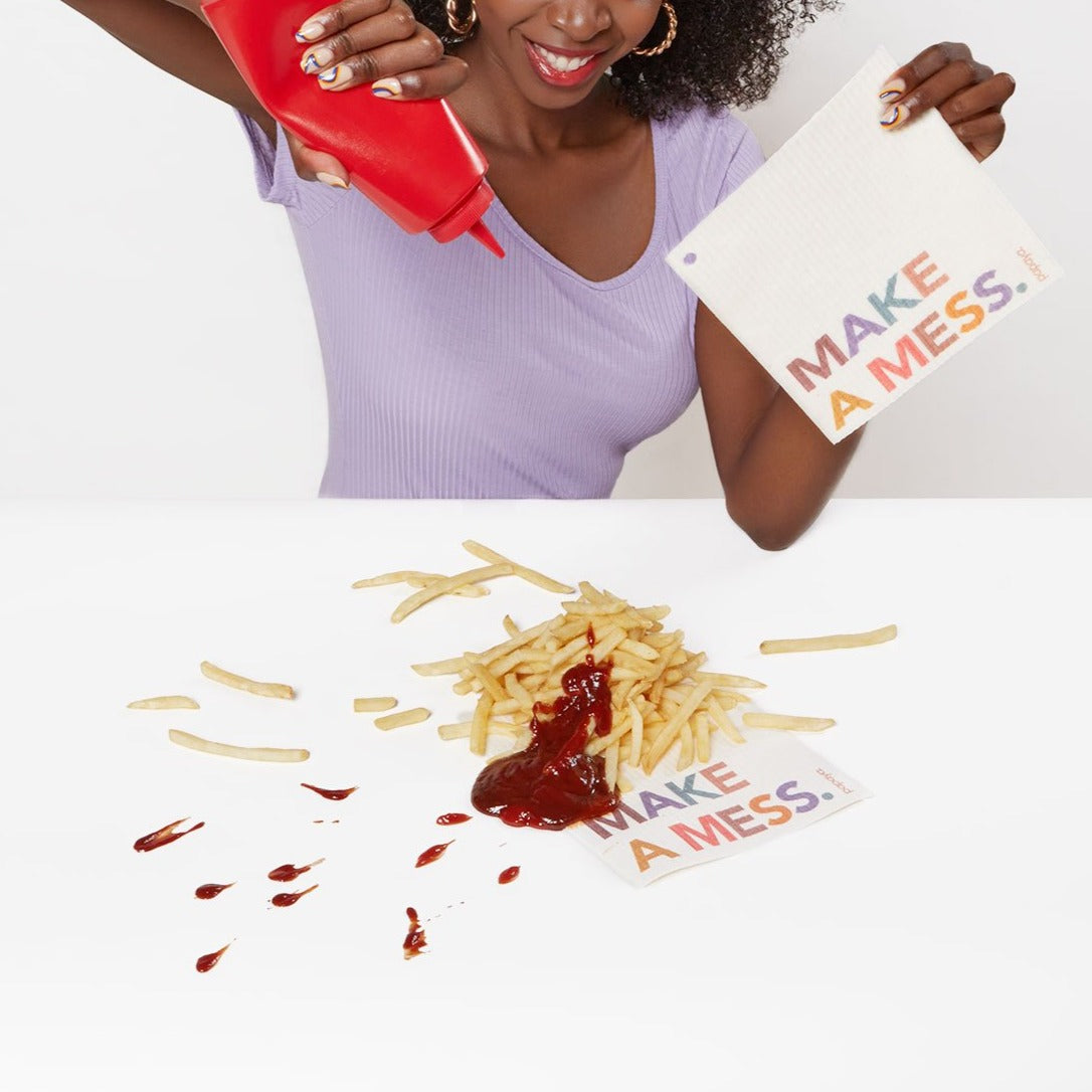 Reusable paper towel that says Make A Mess on a table covered in french fries and ketchup
